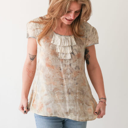 A woman wears a cream silk sleeveless silk top with a three tiered frill at the neck which has been eco printed with pale brown eucalyptus and tea leaves