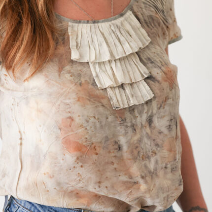 A woman wears a cream silk sleeveless silk top with a three tiered frill at the neck which has been eco printed with pale brown eucalyptus and tea leaves frill detail