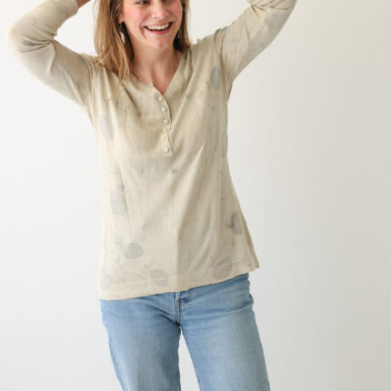A woman wears a grey/cream silk cotton and cashmere long sleeved jersey top with V neck and buttons half way down the front. It has been printed with lilac cotinus leaf eco prints