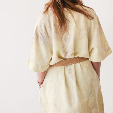 Woman wears pale lemon yellow shift dress (with belt - model's own) eco printed with pale brown eucalyptus prints back view